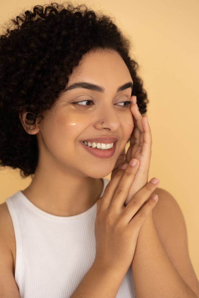 Portrait of a smiling woman gently applying skincare cream on her cheek.