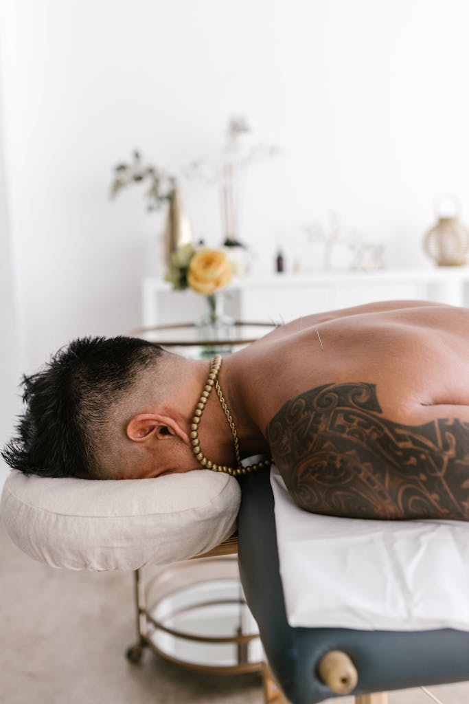 Tattooed man lying face down on a massage table in a spa setting for relaxation and wellness.