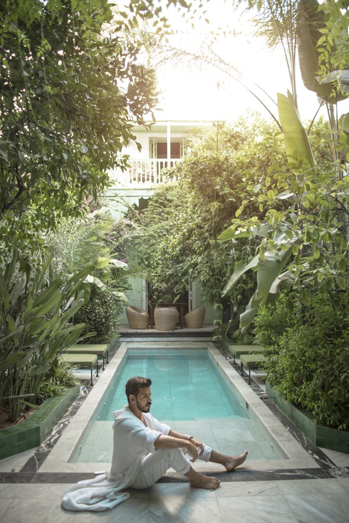 Man relaxing by a serene pool surrounded by lush greenery in a Moroccan setting.